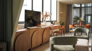 A modern hotel room with a large flat-screen TV, wooden furniture, and a view through large windows.