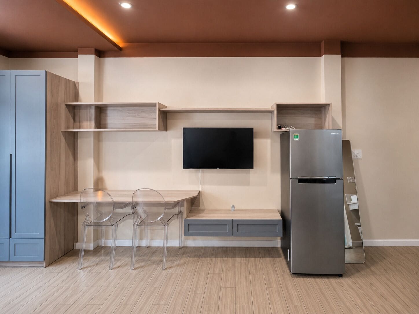 A compact kitchen with a built-in TV, a refrigerator, and a dining area with chairs.