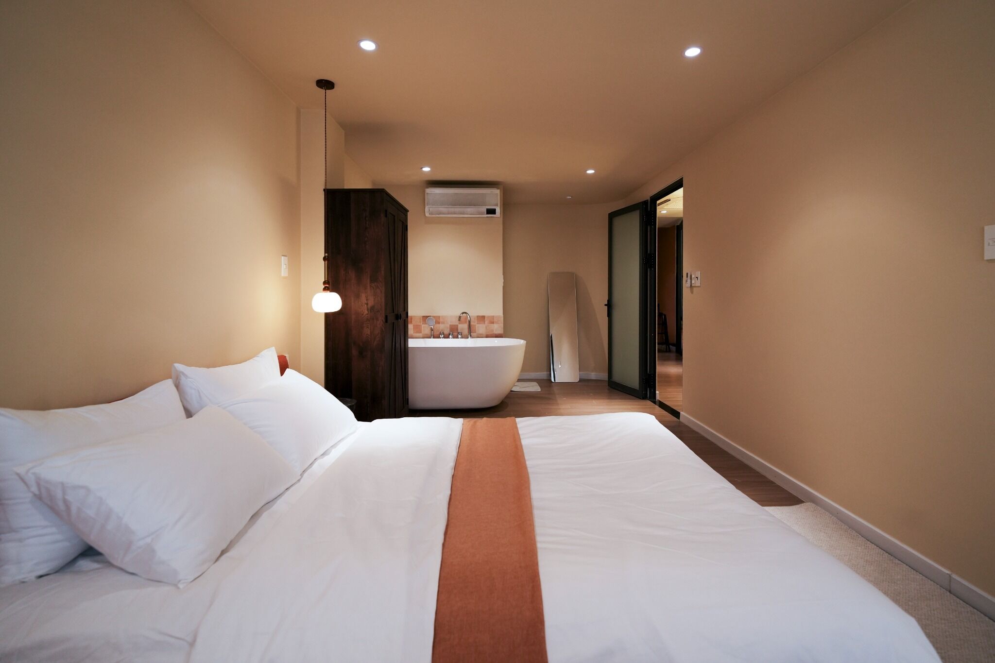 A hotel room with a large bed, a bathroom with a bathtub, and a hallway leading to another room.