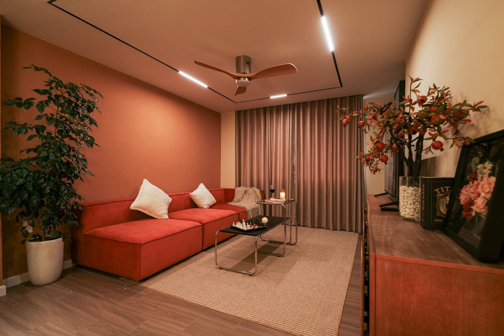 A modern living room with a red sofa, a coffee table, a ceiling fan, a potted plant, and a TV on a wooden stand.