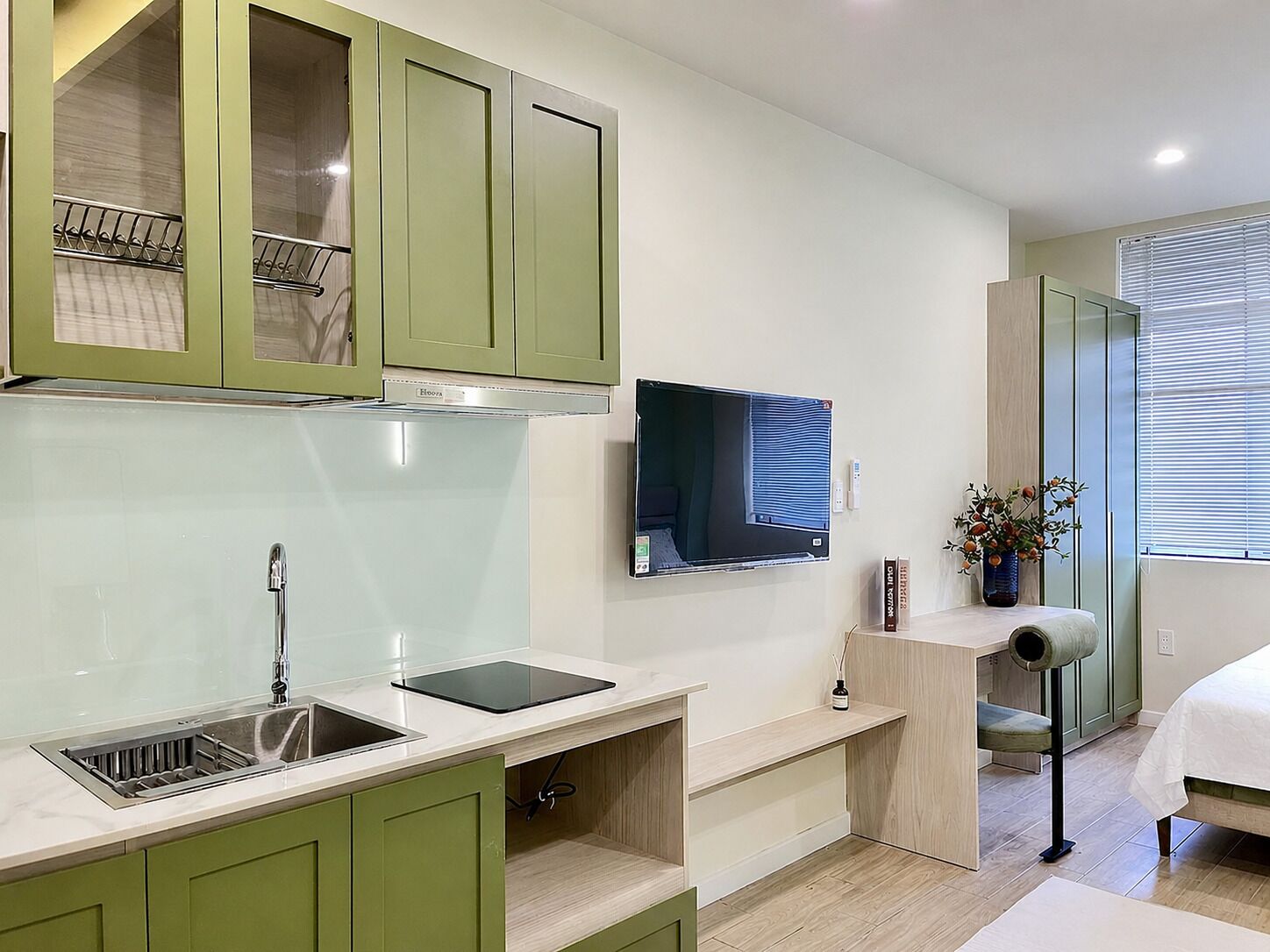 A modern kitchen with green cabinets, a built-in sink, a countertop with a tablet, and a TV mounted on the wall.