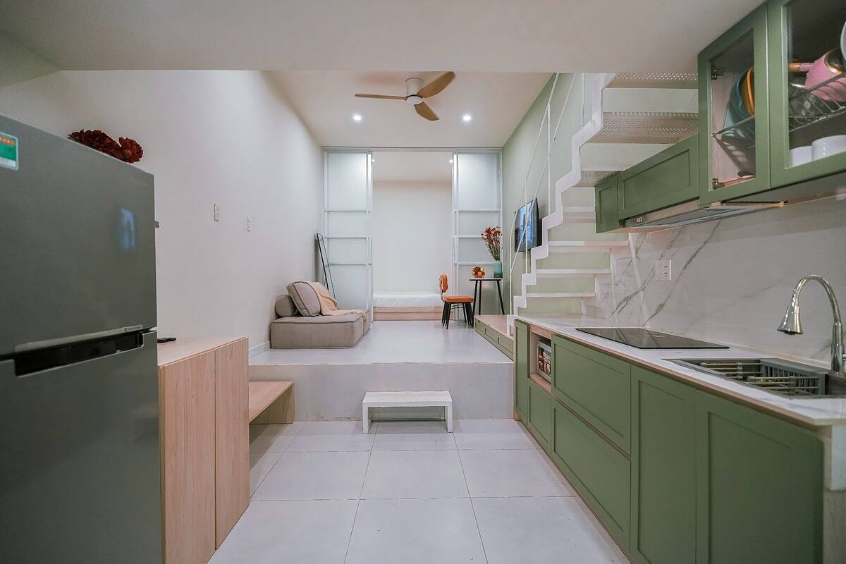A modern kitchen with a built-in refrigerator, a dining area with a sofa, and a staircase leading to an upper level.