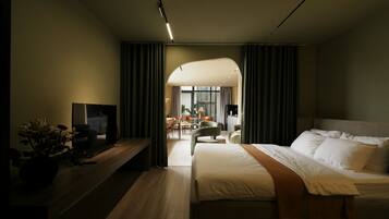 A modern hotel room with a large bed, a desk, and a view into the dining area.