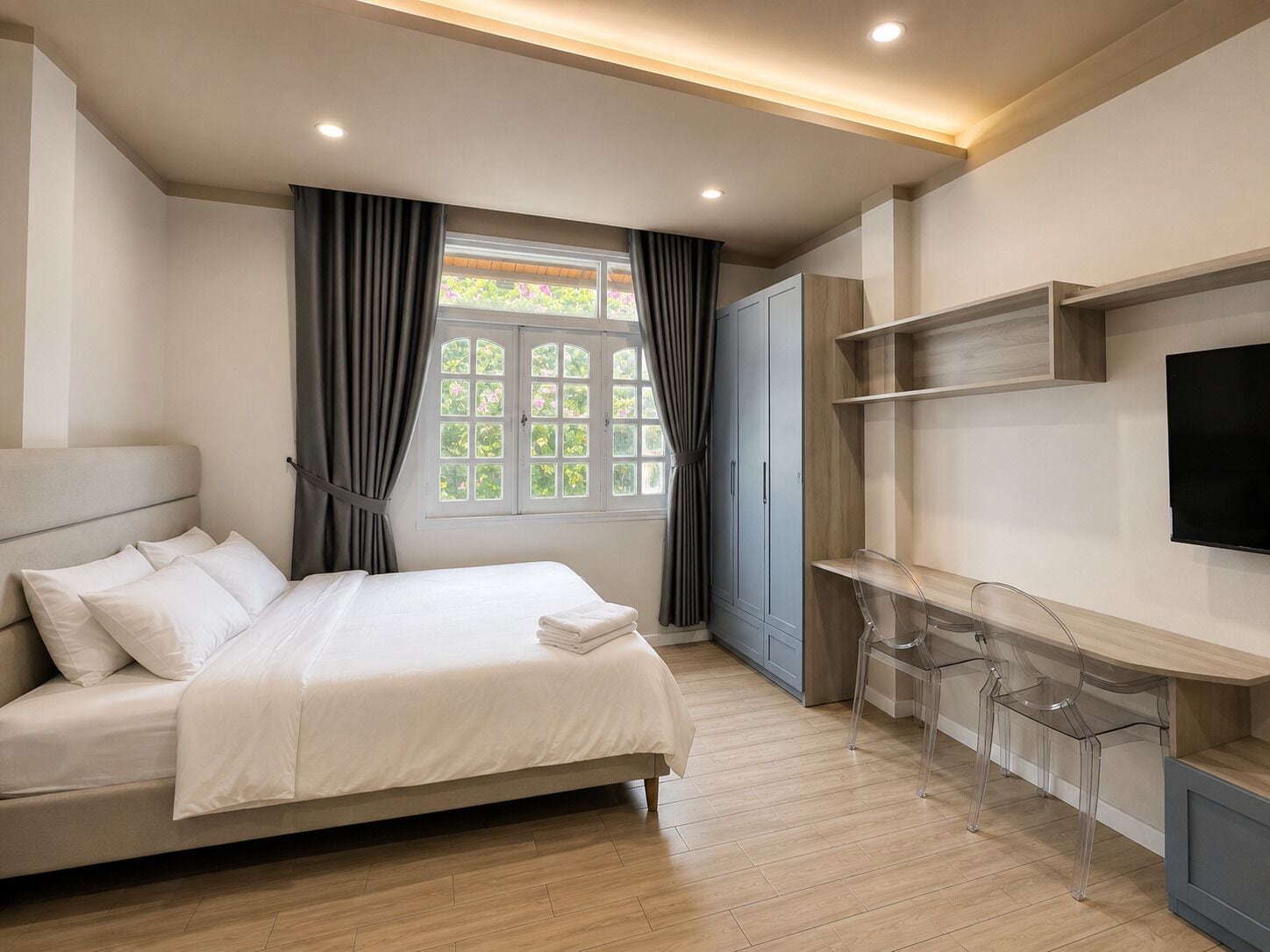 Um quarto moderno com cama, cortinas, televisão e uma mesa com cadeiras.