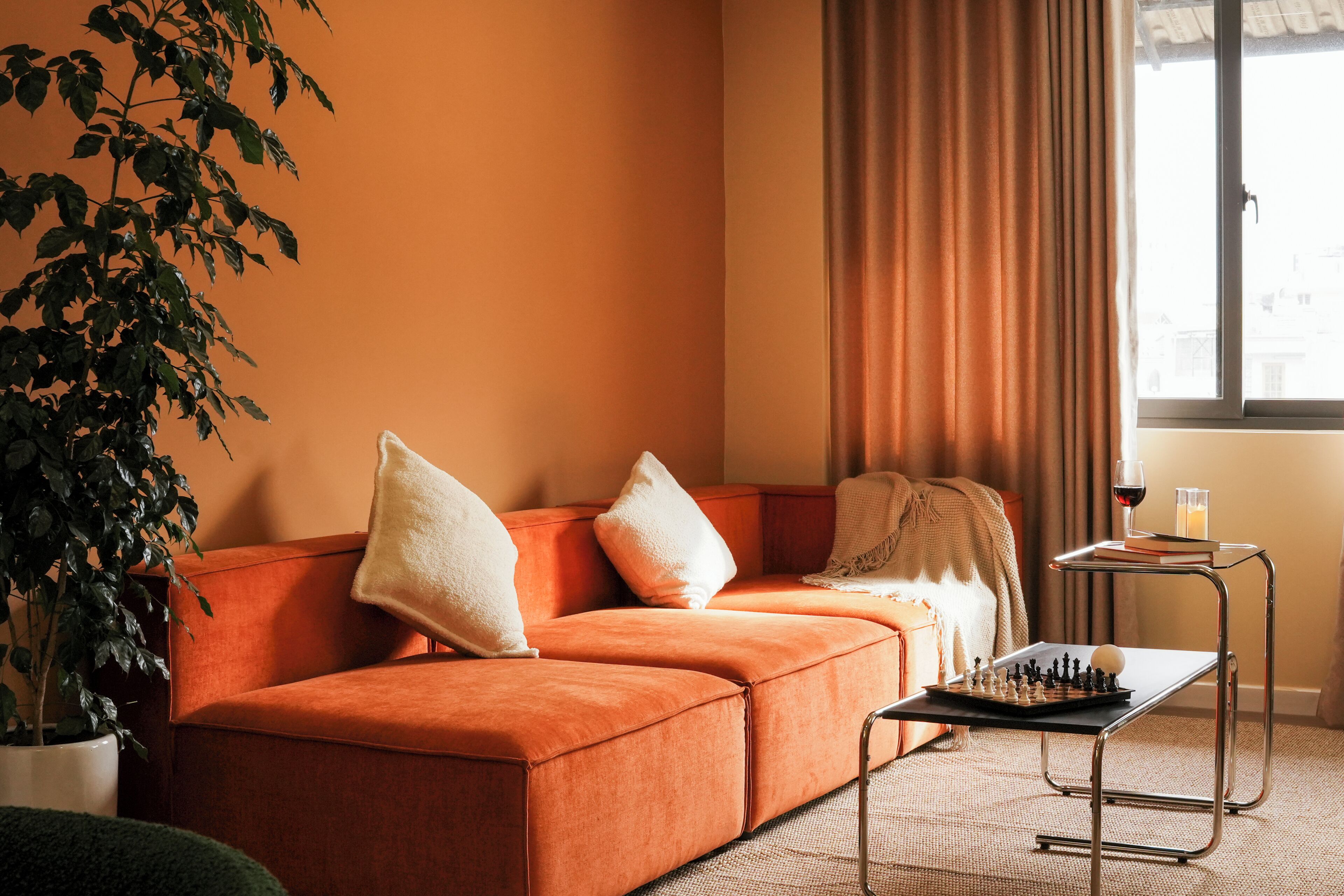 Una sala de estar acogedora con un sofá, una mesa de ajedrez, una planta en maceta y una ventana con cortinas.