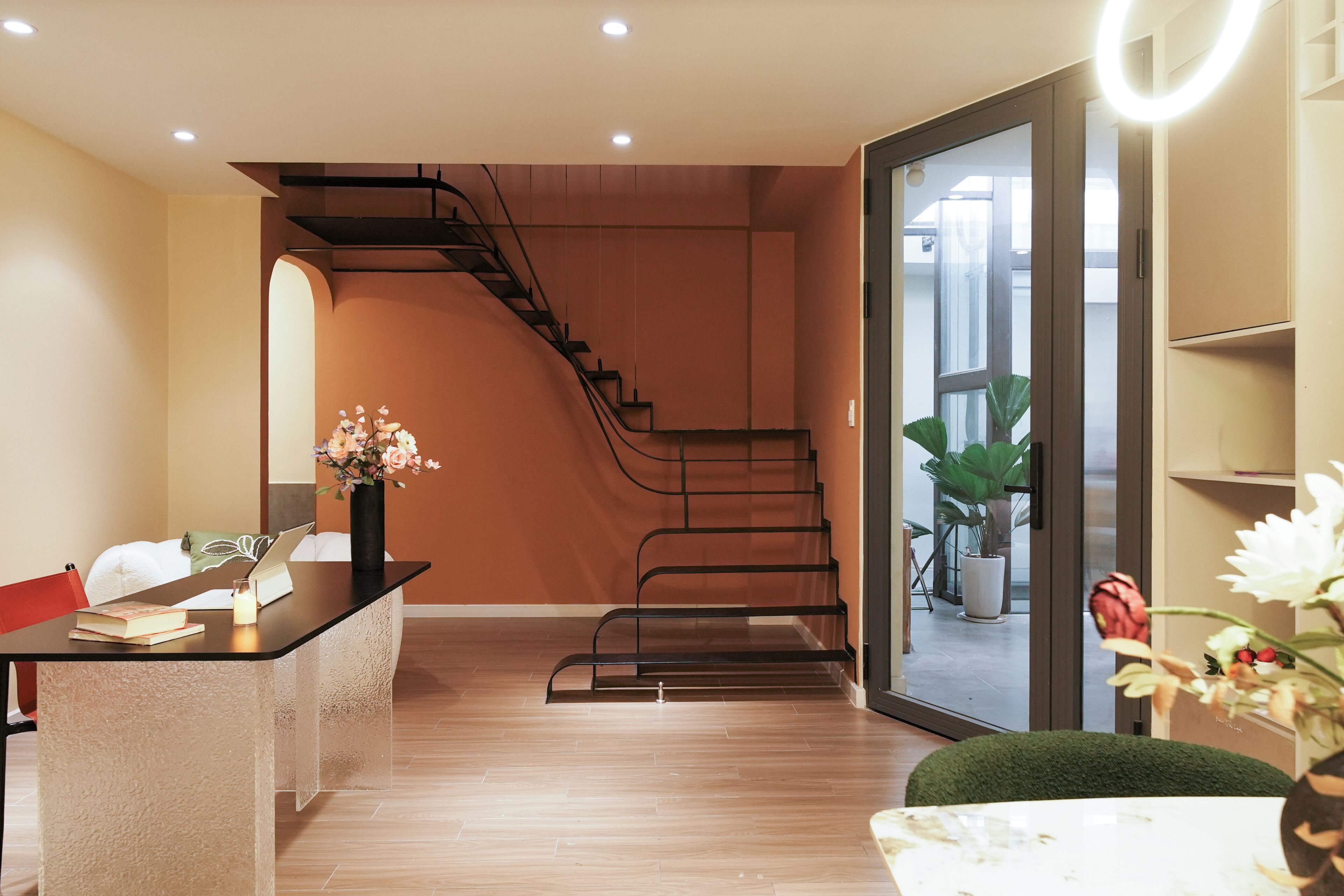 Un intérieur moderne avec un escalier, un bureau agrémenté d’un vase de fleurs et une vue à travers une porte vitrée.