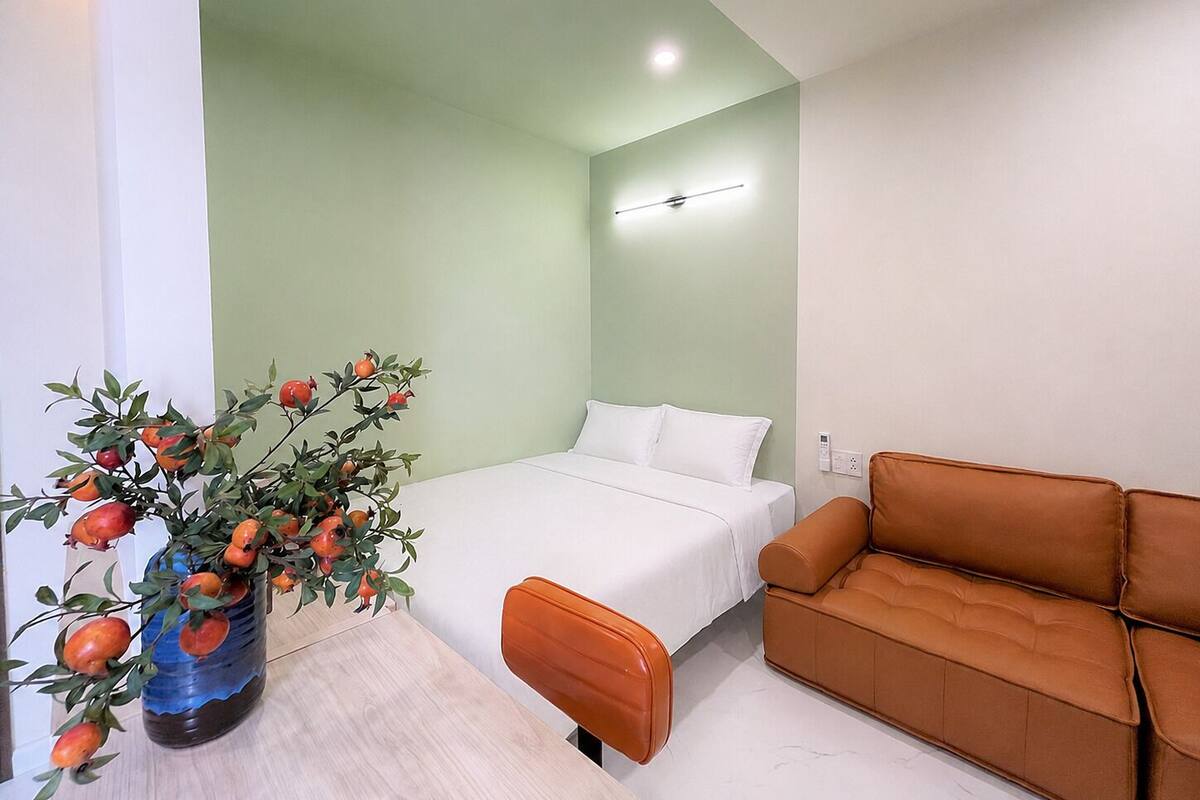A hotel room with a bed, a sofa, a vase with potted plant, and a wall-mounted light.