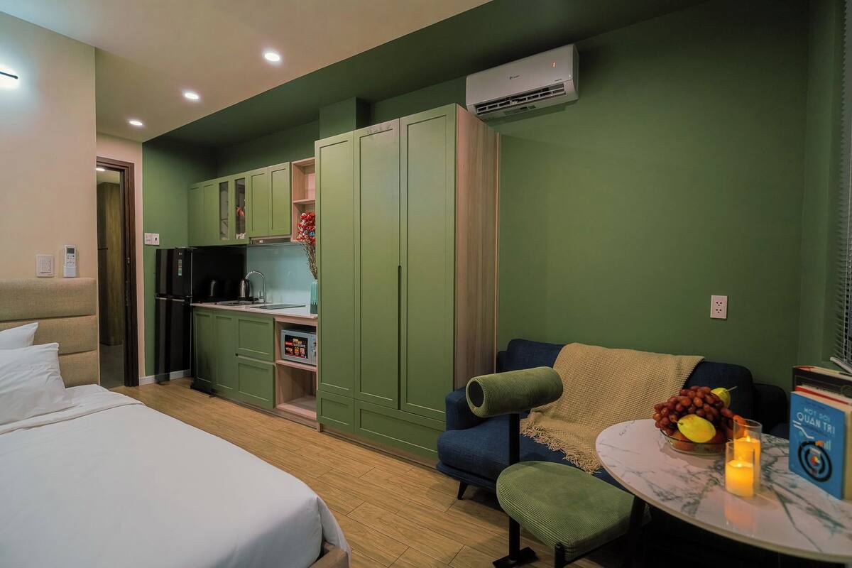 A compact hotel room with a bed, kitchenette, green walls, and a small seating area with a table.