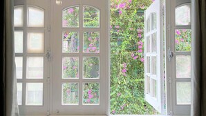 Una habitación con un ventanal grande de varios cristales, una puerta blanca y vistas a un jardín lleno de flores rosas.