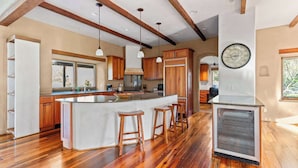A spacious kitchen with wooden cabinets, a large island with stools, pendant lighting, and a built-in refrigerator. - Elegant Cobb House w/ Spa | Pond | Chef Kitchen (Kenwood)