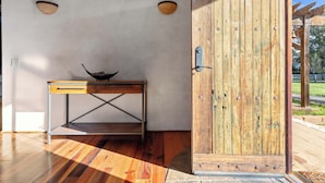 A wooden door with a metal handle, a rustic wooden table with a bowl on top, and a light fixture on the wall. - Elegant Cobb House w/ Spa | Pond | Chef Kitchen (Kenwood)