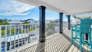 A wooden deck with a railing, a turquoise chair, and a view of a swimming pool and houses in the background. - Shore Thing Getaway | 1 PM Check in! | Large Private Pool & Pergola! | One Block to the New Tarpon Beach Park! | Crystal Beach Gem, Sleeps 22 (Destin)