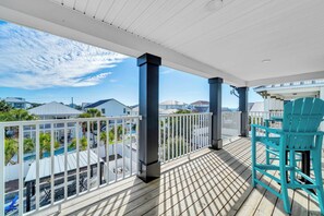 A wooden deck with a railing, a turquoise chair, and a view of a swimming pool and houses in the background. - Shore Thing Getaway | 1 PM Check in! | Large Private Pool & Pergola! | One Block to the New Tarpon Beach Park! | Crystal Beach Gem, Sleeps 22 (Destin)