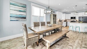 A modern kitchen with white cabinets, a wooden dining table, and a hanging light fixture. - Shore Thing Getaway | 1 PM Check in! | Large Private Pool & Pergola! | One Block to the New Tarpon Beach Park! | Crystal Beach Gem, Sleeps 22 (Destin)