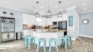 A modern kitchen with white cabinets, a large island with stools, hanging pendant lights, and a backsplash with a mosaic tile pattern. - Shore Thing Getaway | 1 PM Check in! | Large Private Pool & Pergola! | One Block to the New Tarpon Beach Park! | Crystal Beach Gem, Sleeps 22 (Destin)