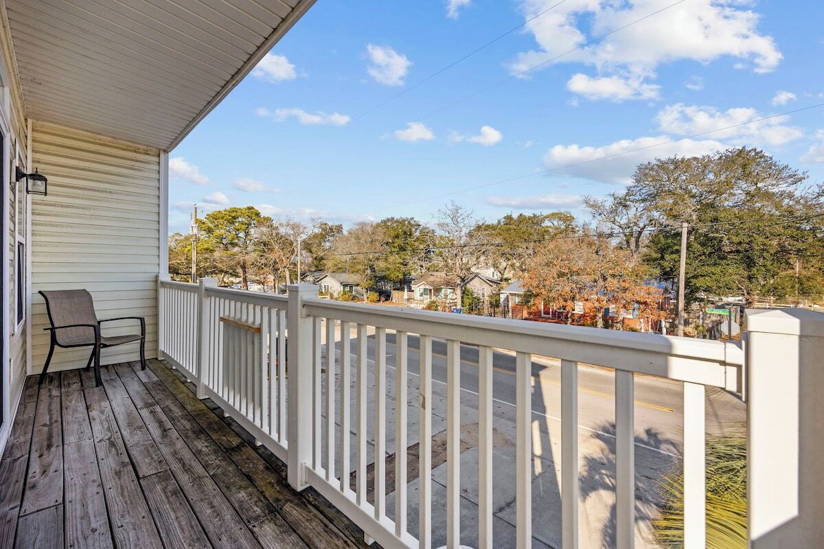 A wooden porch with a white railing, a chair, and a view of a residential street.