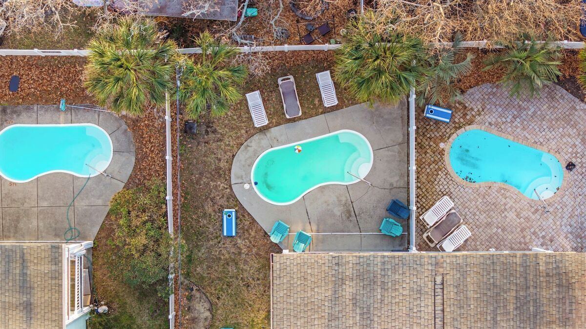 Vista aérea de una zona residencial con tres piscinas, rodeada de palmeras y un paseo pavimentado.