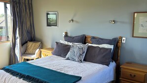 Un dormitorio con cama, una silla, mesita de noche, cómoda y ventana con cortinas.