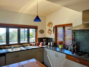 A modern kitchen with a large window, a sink, and a stove. - Across the road from Omanu/Arataki: convenient, relaxing, with beach adventures. (Mount Maunganui)