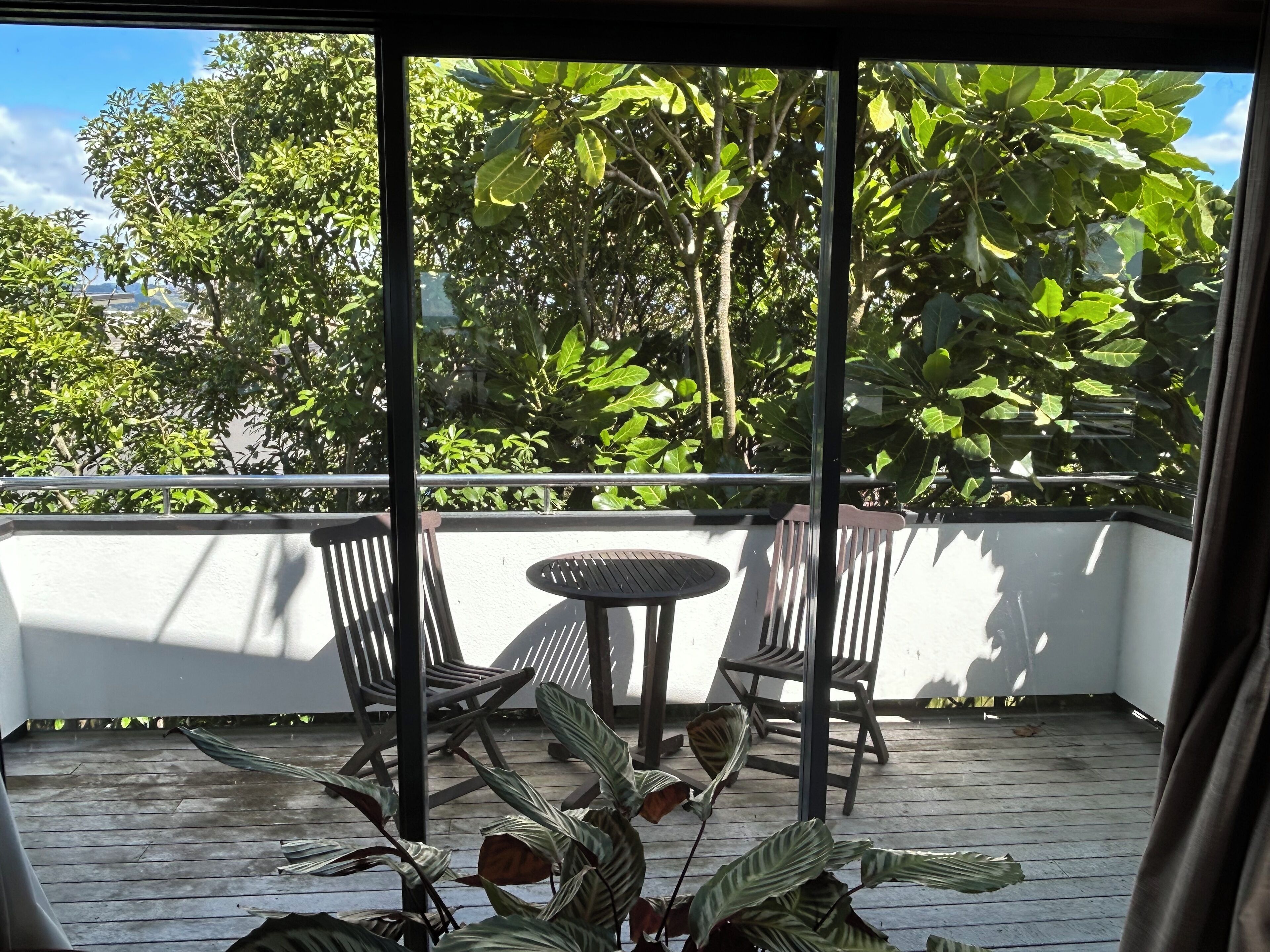 A balcony with a table and chairs, surrounded by lush greenery and trees.