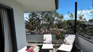 Una terraza de madera con dos sillones de descanso y una mesita, rodeada de plantas en macetas y un veleta.