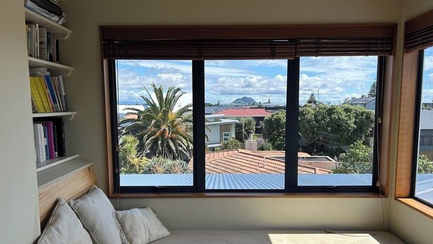 Una habitación con una cama, una estantería y un ventanal con vistas a edificios y árboles.