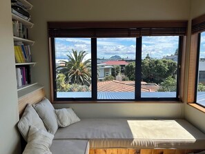 Ein Zimmer mit einem Bett, einem Bücherregal und einem großen Fenster mit Blick auf Gebäude und Bäume.