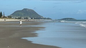 Una playa con gente caminando, una montaña al fondo y cielo despejado.