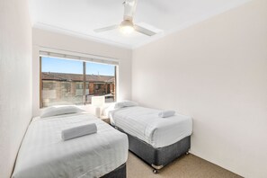 A bedroom with two beds, a ceiling fan, and a window with a view of buildings outside.