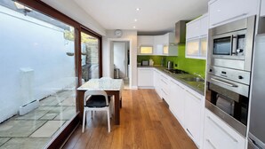 A modern kitchen with white cabinets, a dining table, and a view of the backyard through glass doors. - Contemporary 2BDR City Retreat (Dublin)