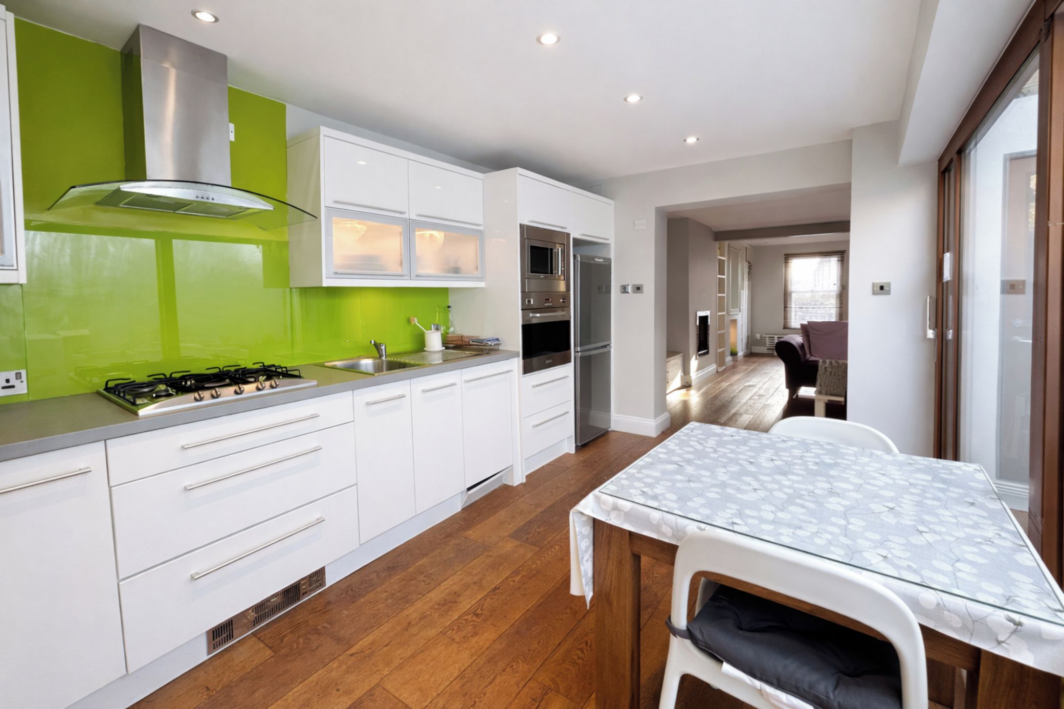 A modern kitchen with white cabinets, a green backsplash, and a dining area with a table and chairs.