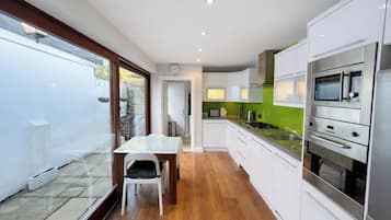 A modern kitchen with white cabinets, a dining table, and a view of the backyard through glass doors.