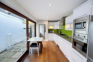 Una cocina moderna con armarios blancos, una mesa de comedor y vistas al jardín trasero a través de puertas de vidrio.