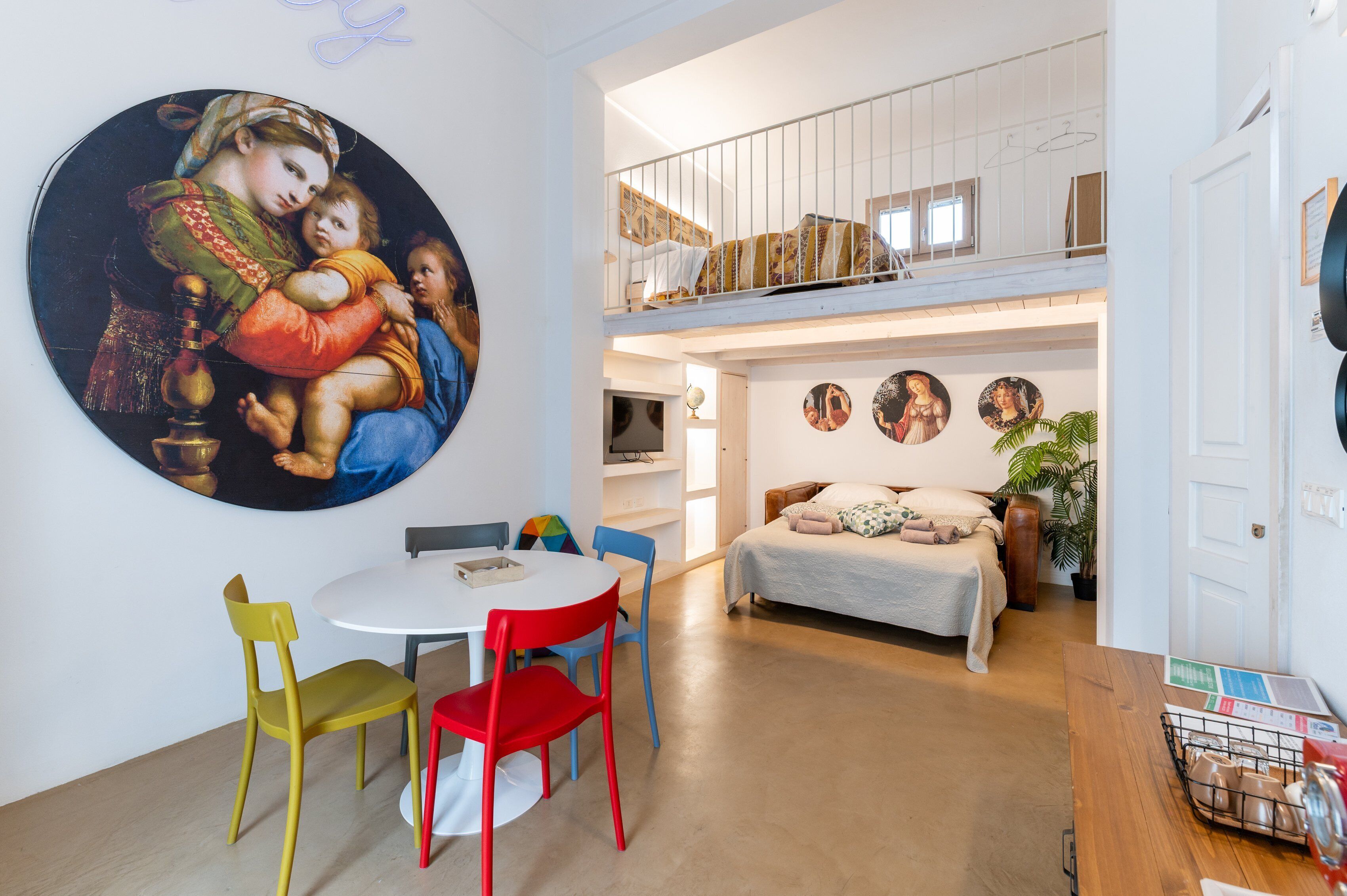 Un interno moderno con zona pranzo, soppalco con camera da letto e un grande quadro appeso al muro.