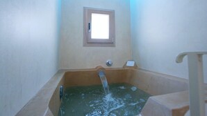 Ein kleiner, schummrig beleuchteter Raum mit einer Badewanne, einem Fenster und einer Tür.