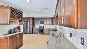 A modern kitchen with wooden cabinets, stainless steel appliances, a granite countertop, and a tiled backsplash. - Coastal Oasis! Hot Tub, Pool & Ping Pong Tables, Fenced Yard, Near Beach! (Port Orange)