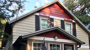 Una casa de dos pisos con techo rojo, una bandera al frente y un buzón.