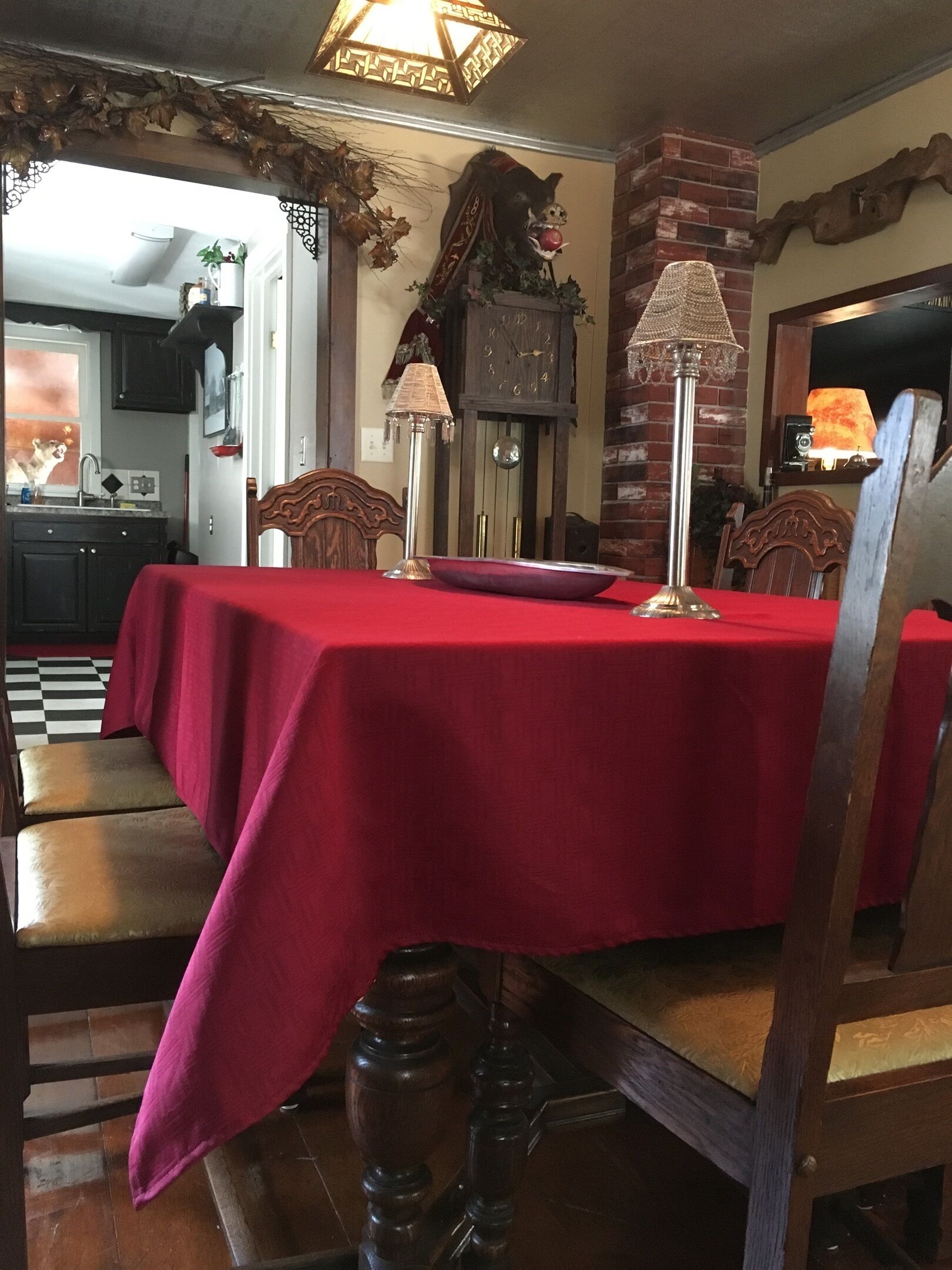Zona pranzo con tovaglia rossa, sedie di legno e un lampadario.
