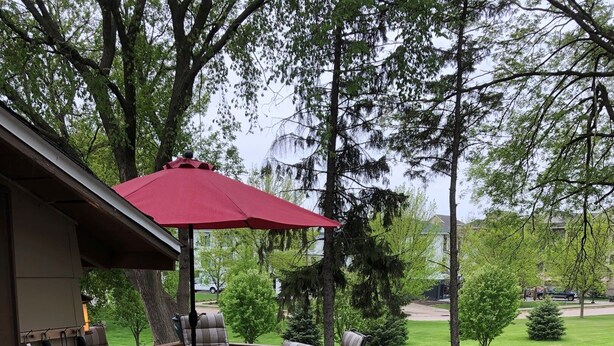 Una terraza de madera con una parrilla, mesa de comedor, sillas y un paraguas rojo.