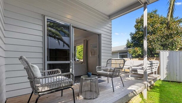 Une véranda avec deux fauteuils en osier et une petite table ronde, une porte-fenêtre coulissante et une terrasse en bois.