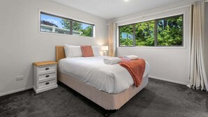 Une chambre à coucher avec un lit, des tables de chevet, une fenêtre et une vue sur la verdure.