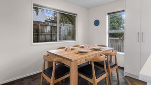 Un coin repas avec une table et des chaises en bois, une fenêtre donnant sur une clôture en bois, et une porte avec un placard intégré.