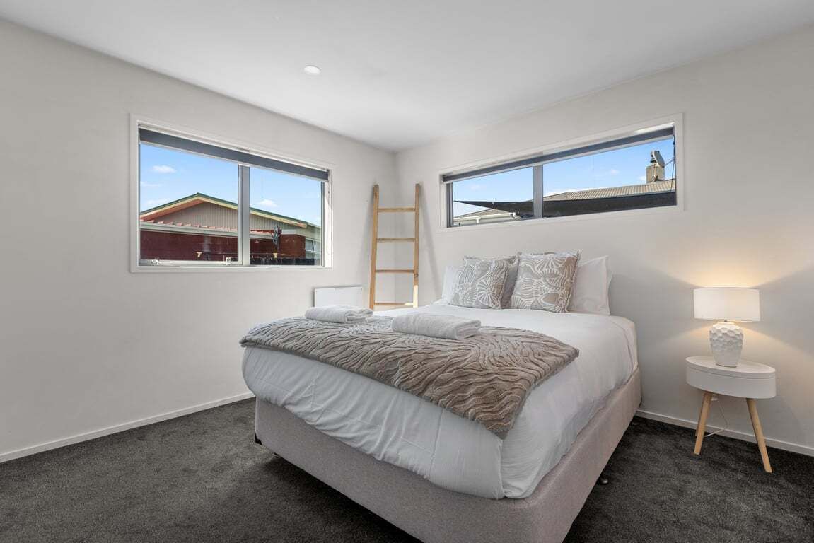 Une chambre à coucher avec un lit, deux fenêtres, une table de chevet et une échelle.
