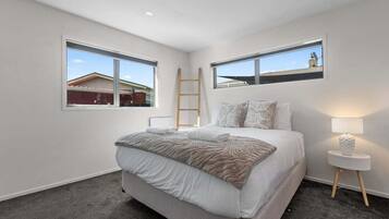 Une chambre à coucher avec un lit, deux fenêtres, une table de chevet et une échelle.