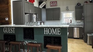 Et køkken med en central ø, skilt med "GUEST HOME", rustfrie stålapparater og et vindue med udsigt.