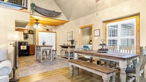 A spacious dining area with a wooden table and benches, a kitchen in the background, and a large window with blinds. - Emerald Point, Lakefront with Gorgeous Views! (McAlester)