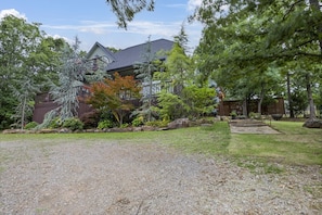 A house with a gravel driveway, surrounded by trees and a wooden deck.