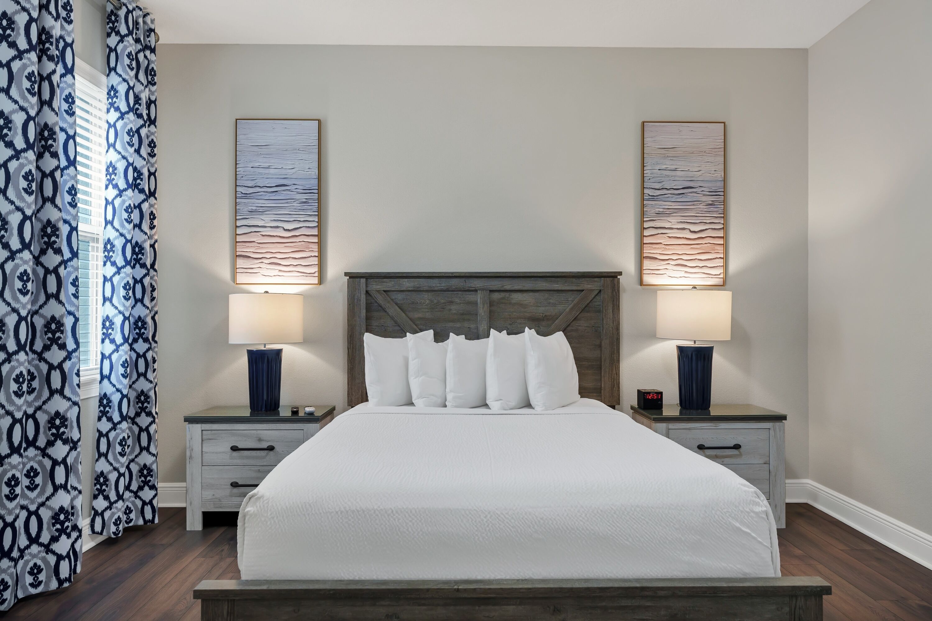 A neatly made bed with a wooden headboard, two bedside tables with lamps, and patterned curtains.