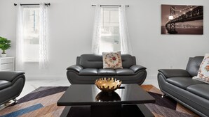 Een moderne woonkamer met een zwarte leren bank, een zwarte salontafel met een gouden schaal, en een stadsgezicht schilderij aan de muur.
