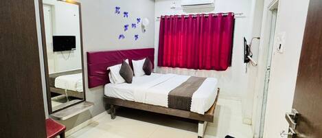 A hotel room with a bed, a mirror, a ceiling fan, an air conditioning unit, and a red curtain.
